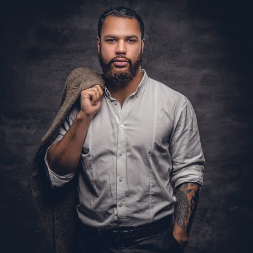 Portrait of bearded black man with tattooed arm wearing white shirt.